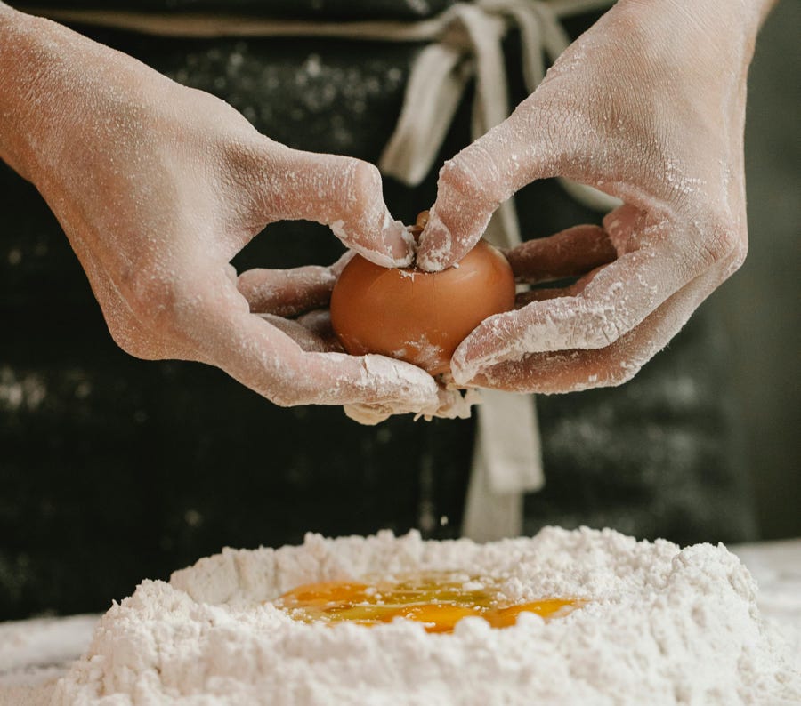 Crop cook breaking egg into flour